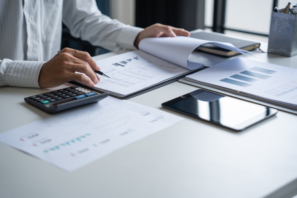 Reviewer checking printed financial records with a pen and calculator at a desk